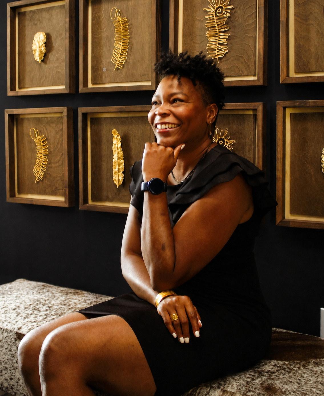 Dawn McCall, founder of Thime Concierge Solutions, seated before a wall of framed gilded botanical studies