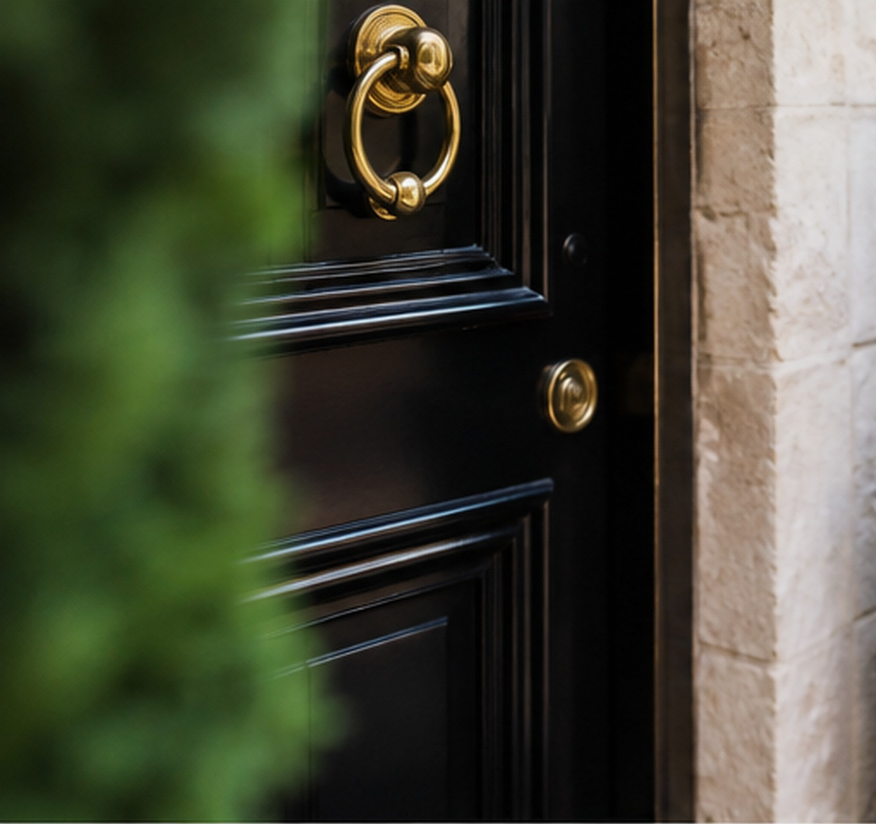 A black panelled front door with a brass ring knocker, set in pale stone
